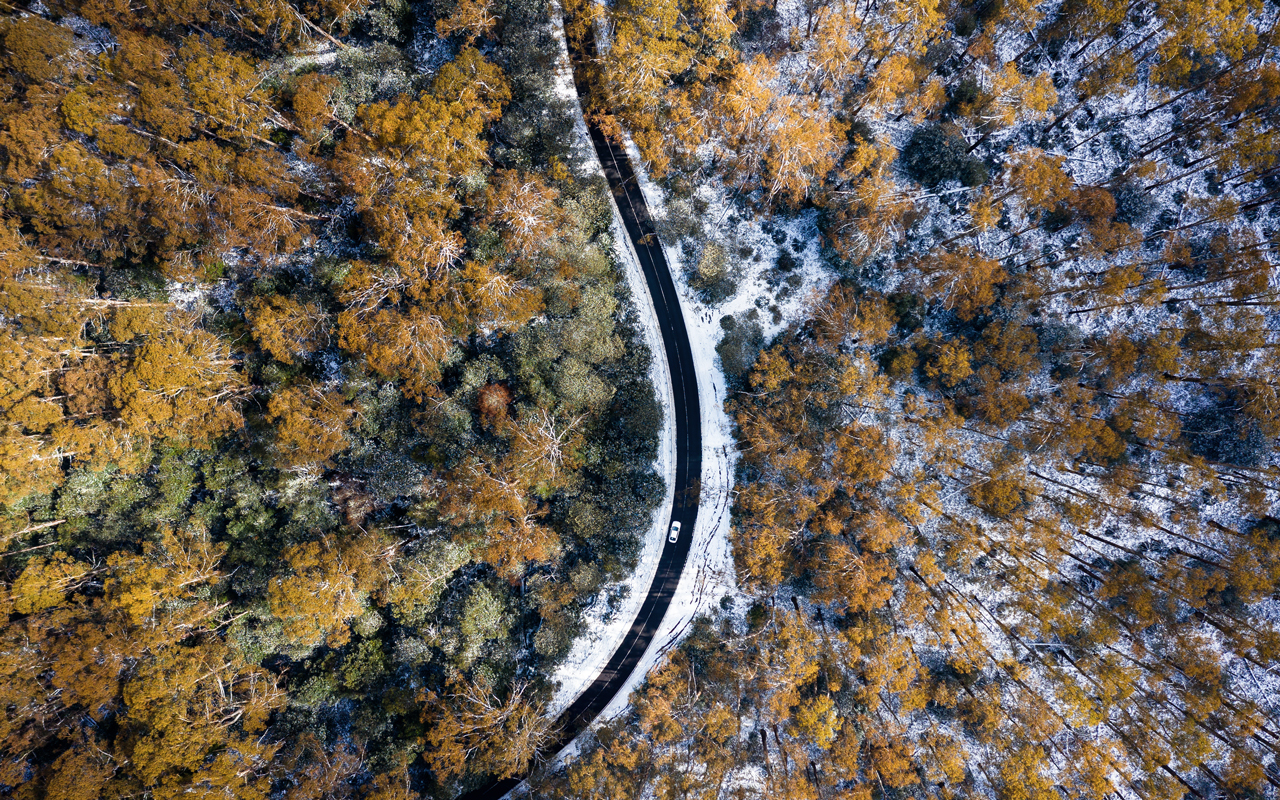 Aerial view of a remote high way. Fall foliage surrounds the highway with snow covered ground.